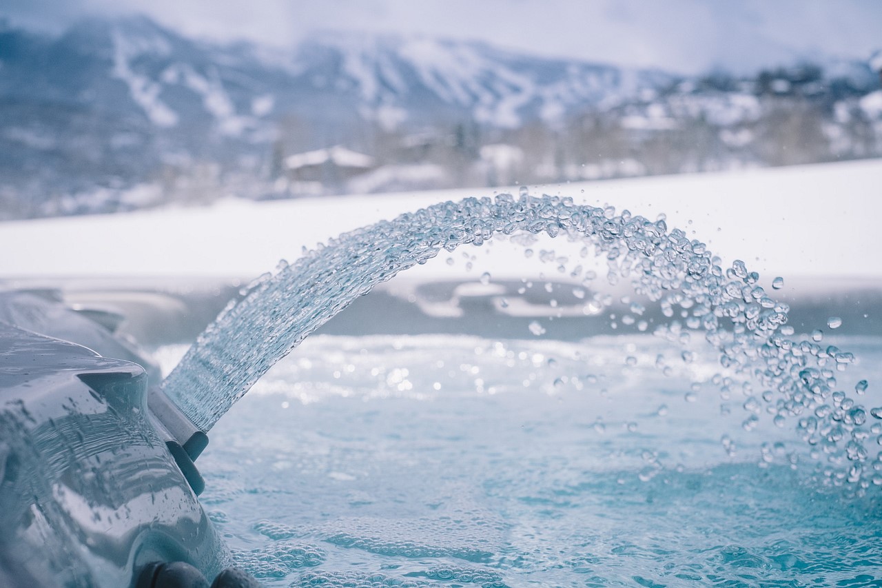 Close view of jet waterfall over Caldera hot tub with snowy mountains in the background